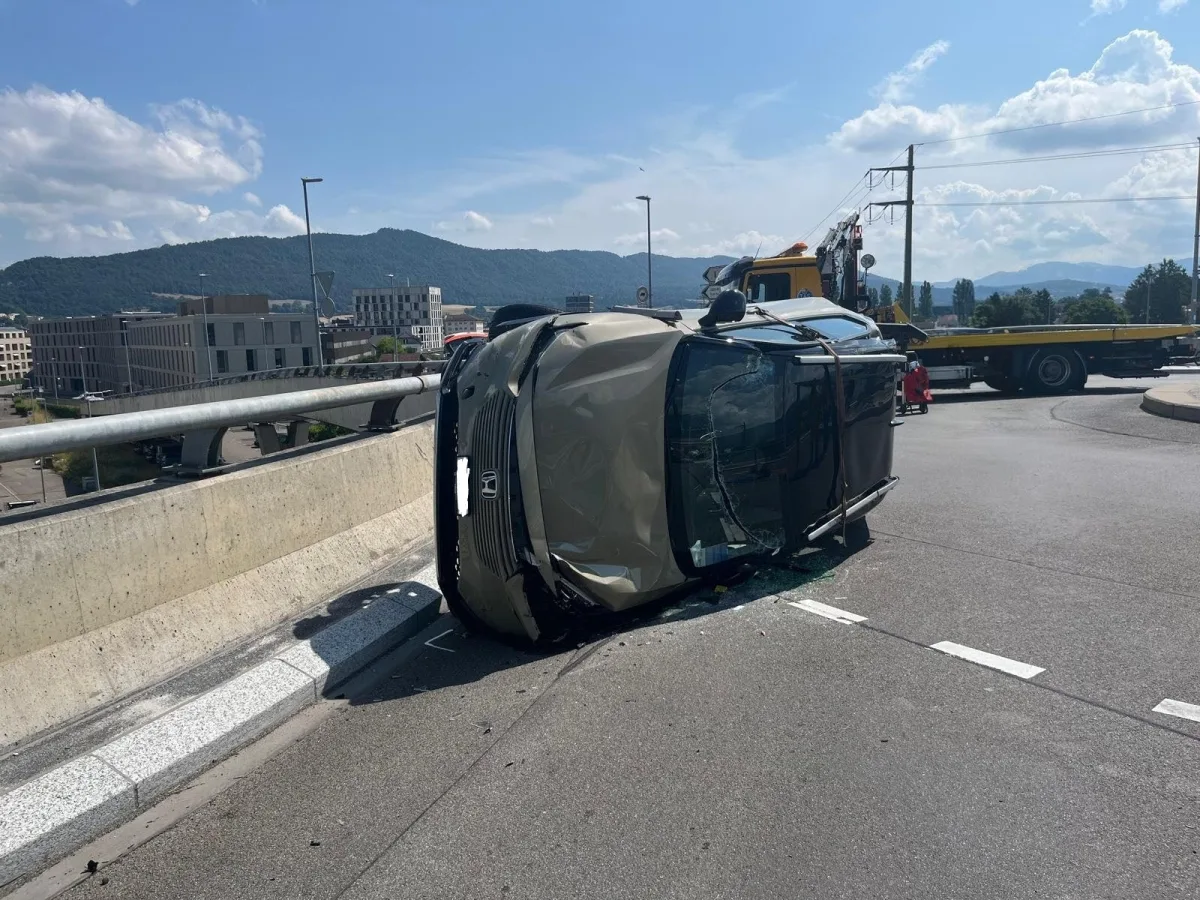 Ein umgekippter PKW liegt auf der Fahrbahn einer Brücke. Im Hintergrund sind Berge und teilweise bewölkter Himmel zu sehen.
