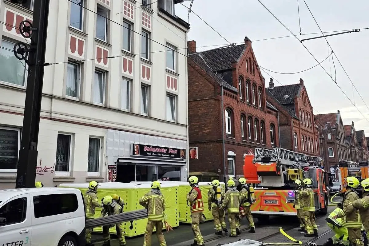 Mehrere Feuerwehrleute sind auf einer Straße in einem urbanen Gebiet im Einsatz, umgeben von Wohngebäuden.