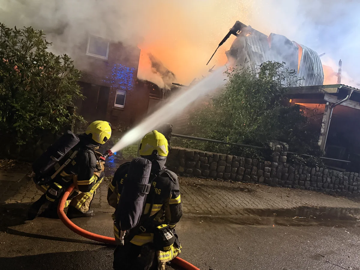 Mehrere Feuerwehrleute kämpfen gegen einen ausgebrochenen Brand in einem Gebäude. Sie verwenden einen Schlauch, um das Feuer zu löschen.