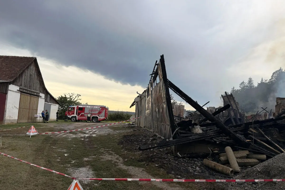 Eine teilweise eingestürzte Scheune wird nach einem Brand untersucht; ein Feuerwehrfahrzeug steht daneben, während Absperrungen den Bereich sichern.