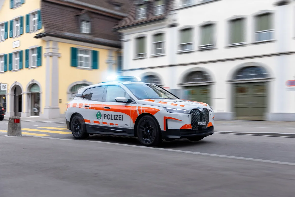 Ein Polizeifahrzeug der Kantonspolizei St. Gallen fährt mit eingeschaltetem Blaulicht durch eine belebte städtische Straße. Im Hintergrund sind ältere Gebäude zu sehen.