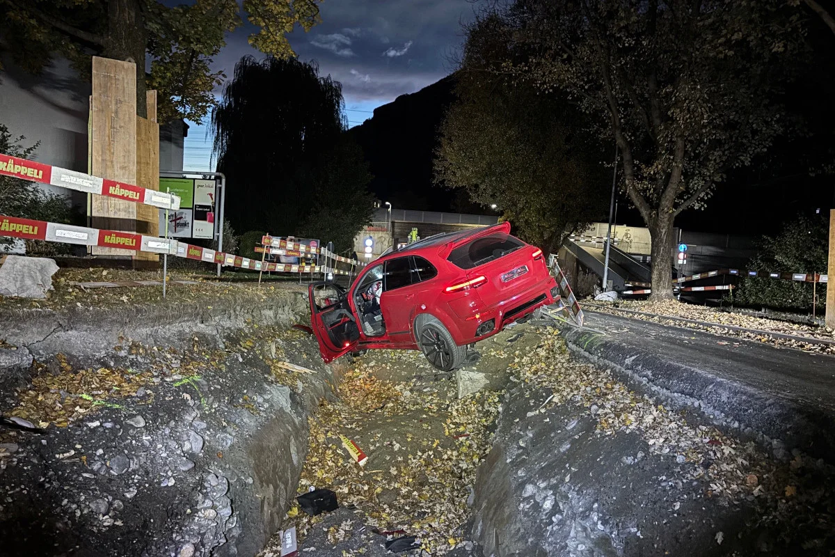 Ein rotes Auto ist in der Nacht in einen Baugraben gerutscht. Die Fahrertür steht offen und das Fahrzeug ist in einem durch Baustellenabsperrungen gekennzeichneten Bereich.