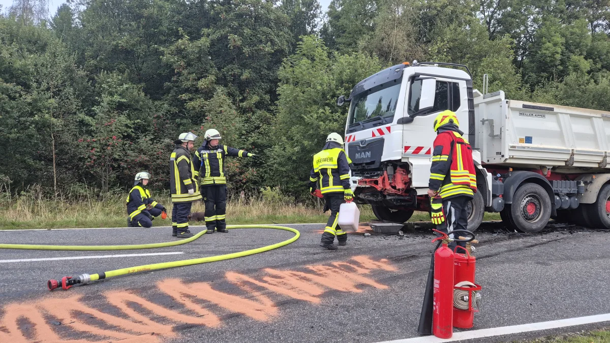 Mehrere Feuerwehrleute sind auf einer Straße neben einem MAN-Lkw aktiv. Sie sind dabei, ausgelaufene Flüssigkeiten zu binden.