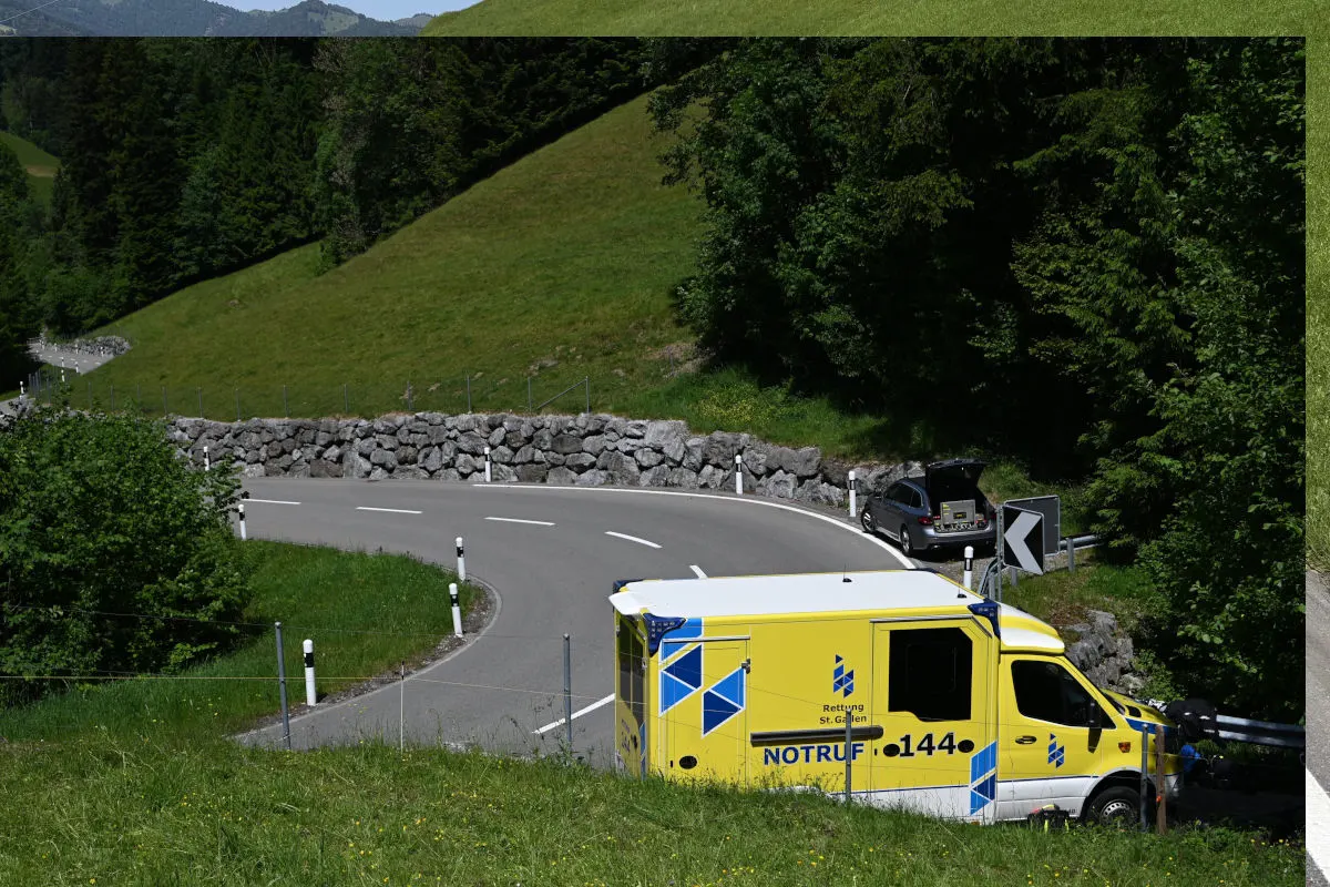Ein gelber Rettungswagen von 'Rettung St. Gallen' steht auf einer kurvigen Straße in bergigem Alpengebiet. Daneben befindet sich ein geparktes Auto am Straßenrand.