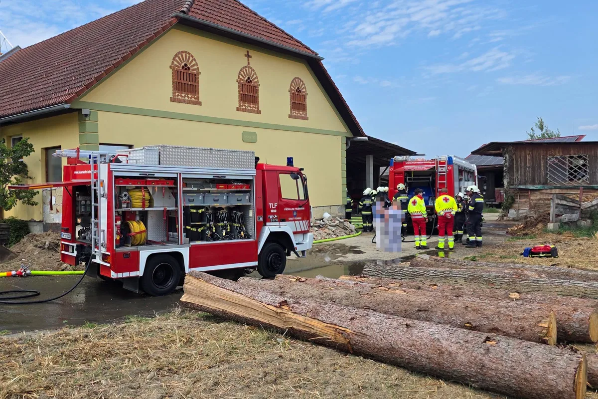 Ein rotes Feuerwehrfahrzeug steht vor einem gelben Gebäude, während Feuerwehrleute und Rettungskräfte tätig sind.
