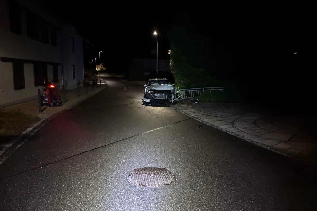 Auf einer nächtlichen Straße ist ein Auto frontal gegen ein Geländer geprallt. Die Straße ist verlassen und schwach beleuchtet.