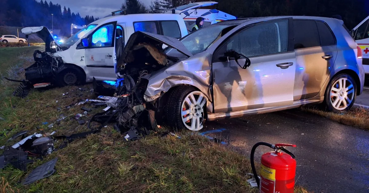 Zwei stark beschädigte Fahrzeuge stehen nach einem Unfall auf einer Straße. Blaulicht eines Einsatzfahrzeugs leuchtet im Hintergrund.
