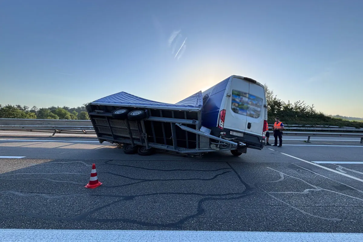 Ein Lieferwagen zieht einen umgekippten Anhänger auf einer leeren Autobahn bei Tagesanbruch. Zwei Personen in Westen stehen daneben.