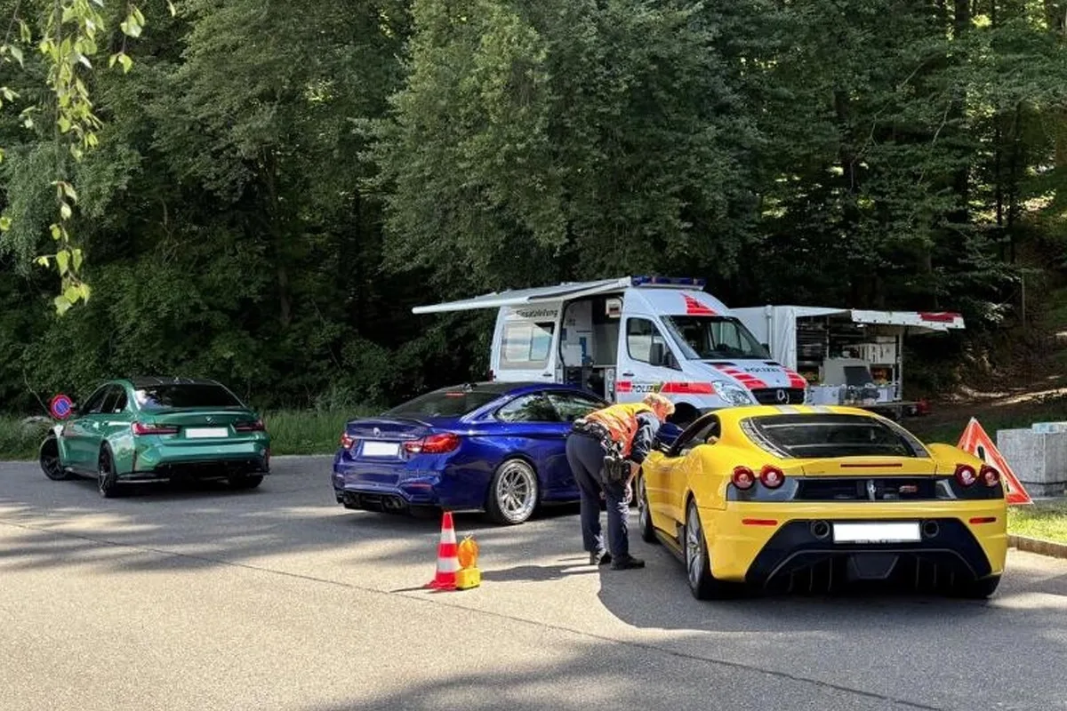 Ein Polizist spricht mit dem Fahrer eines gelben Sportwagens neben mehreren Autos auf einer Landstraße. Im Hintergrund steht ein Polizeifahrzeug.