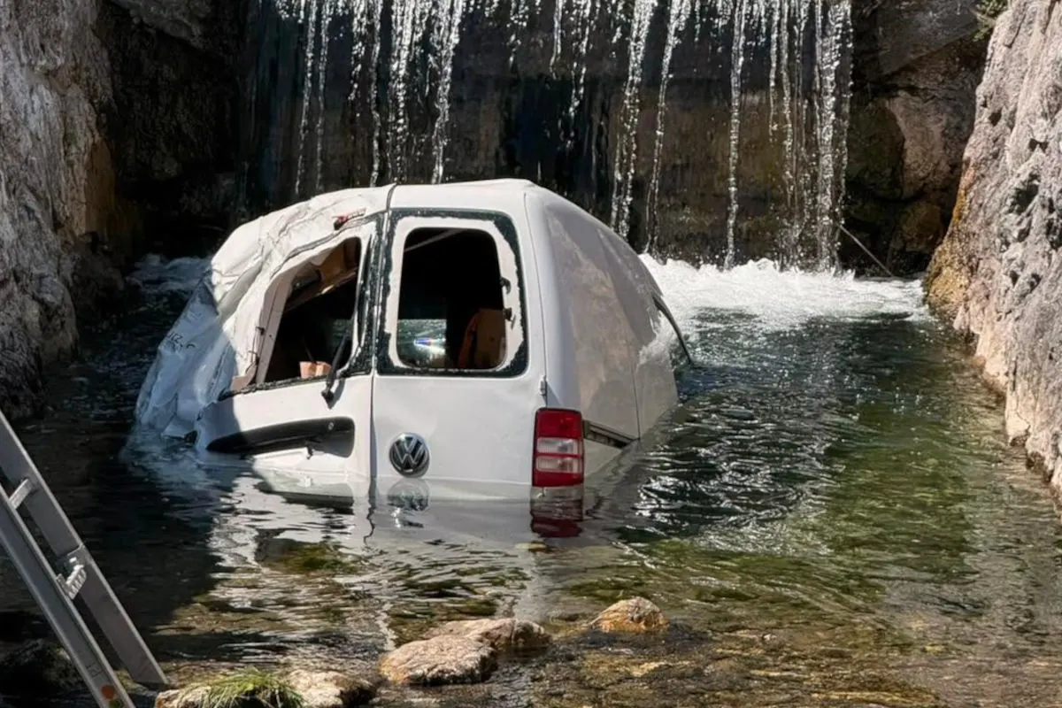 Ein weißer VW-Transporter ist im Wasser unter einem kleinen Wasserfall eingeklemmt. Das Fahrzeug ist beschädigt und halb untergetaucht.