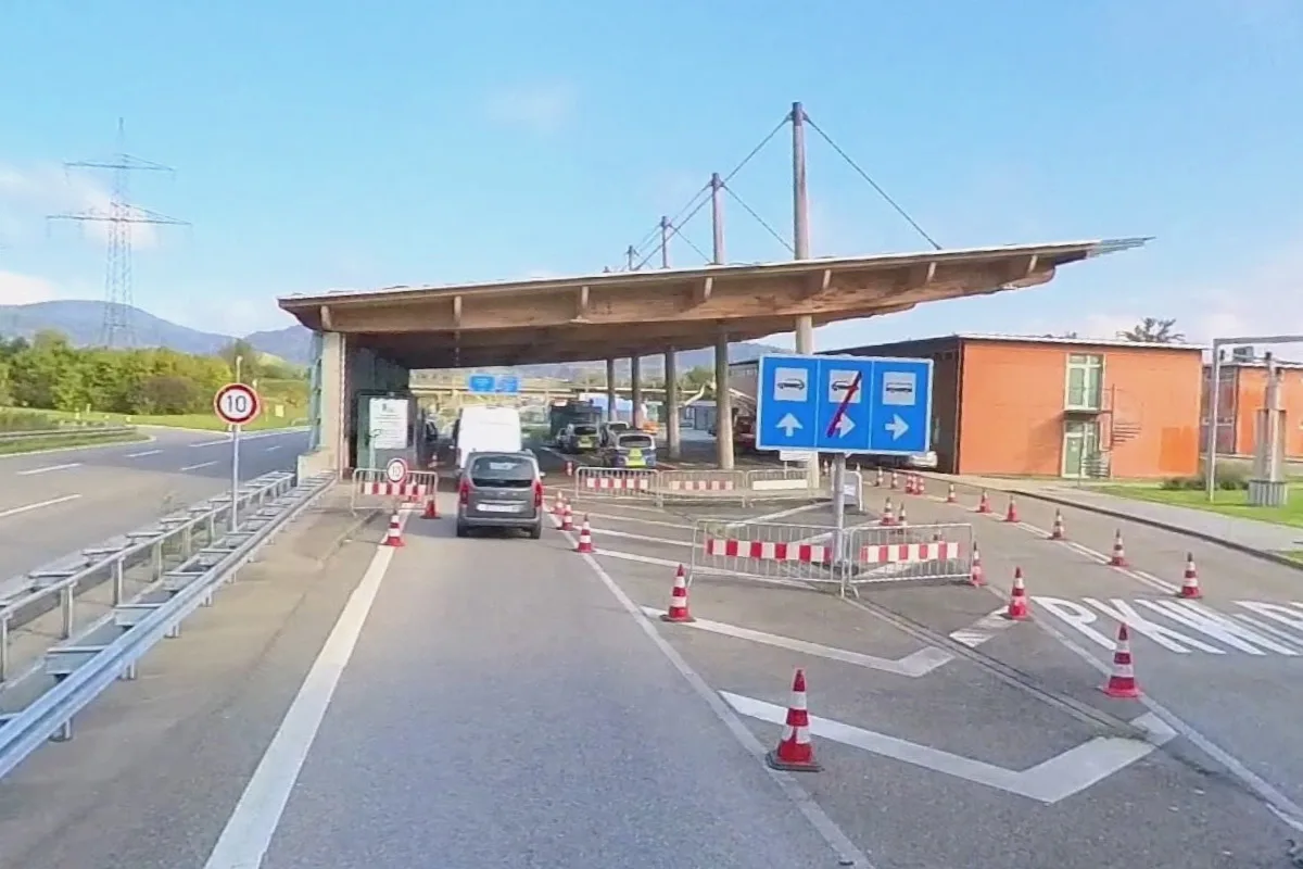 Ein Grenzkontrollpunkt mit mehreren Fahrspuren, Leitkegeln und Verkehrsschildern bei Tageslicht. Autos warten oder fahren durch die Station.