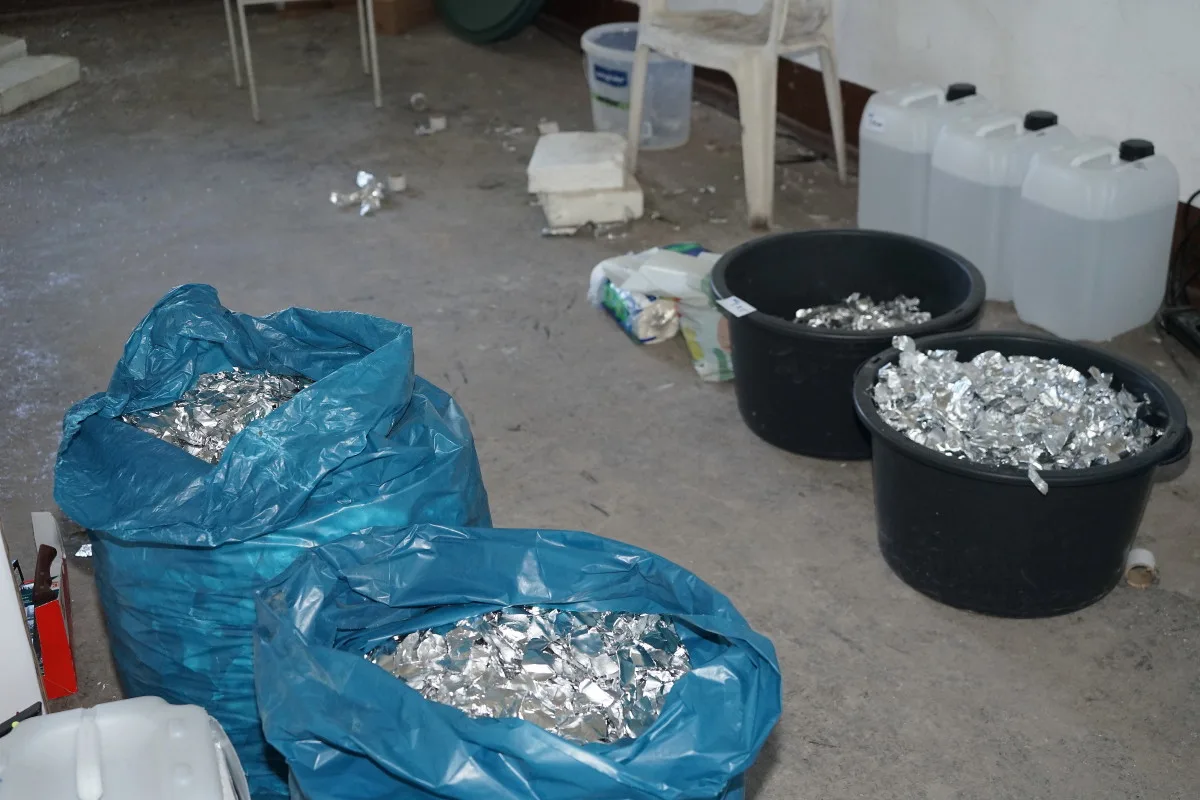 Mehrere Plastiksäcke und Behälter sind gefüllt mit Aluminiumfolie und stehen in einem unordentlichen Lagerraum, der Anzeichen intensiver Nutzung aufweist.