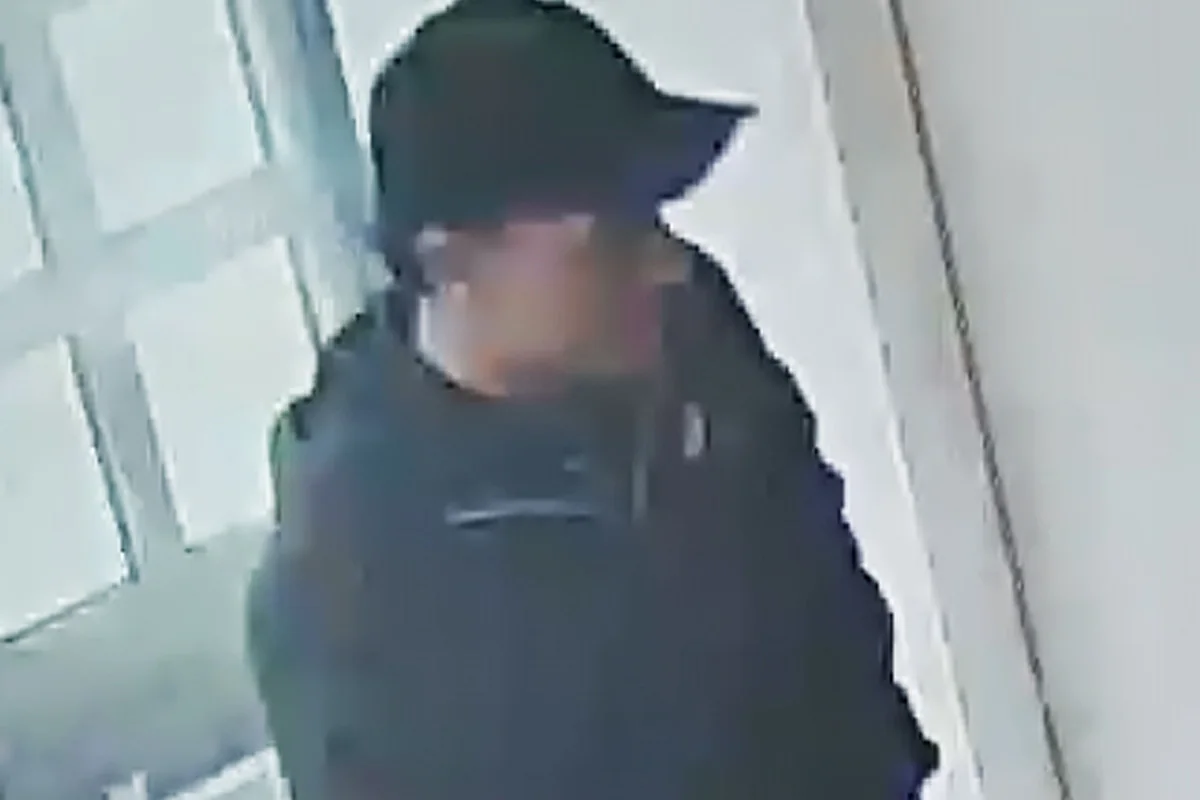 Eine Person in dunkler Kleidung und einer Basecap steht in einem Gebäude, von einer Überwachungskamera aufgenommen.