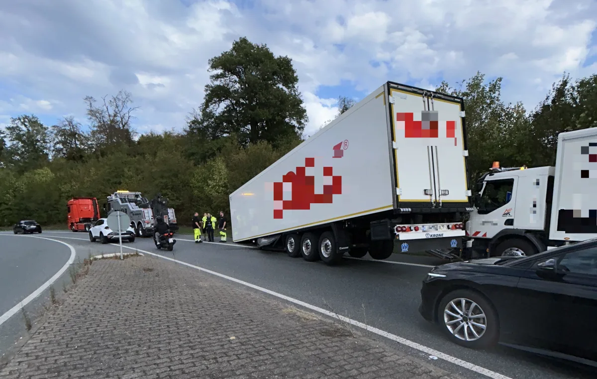 Ein weißer Lkw mit Anhänger steht auf einer Straße, flankiert von mehreren Einsatzfahrzeugen. Menschen in Warnwesten sind vor Ort.