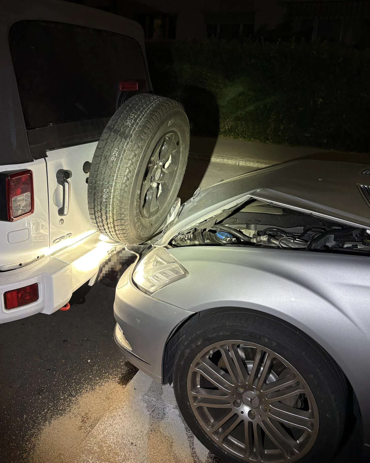 Bei Nacht ist ein silbernes Auto auf das Heck eines weißen Geländewagens aufgefahren, wobei Schäden an der Front des Autos sichtbar sind.