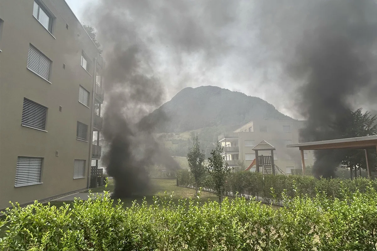 Zwischen zwei Wohngebäuden steigt dichter schwarzer Rauch auf. Ein Spielplatz mit einer Rutsche ist daneben zu sehen.