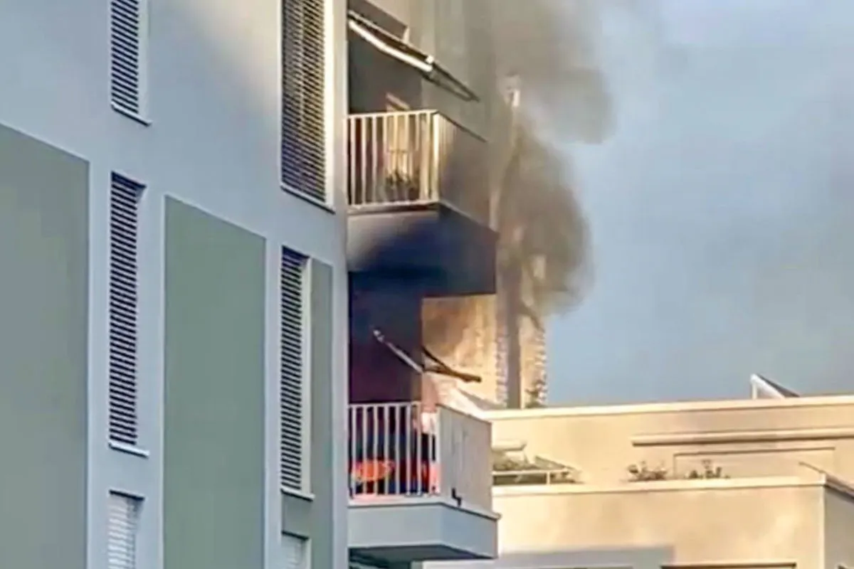 Ein Balkon eines mehrstöckigen Gebäudes ist in Flammen und erzeugt starken Rauch, der nach oben zieht. Die Fassade weist dunkle Brandspuren auf.