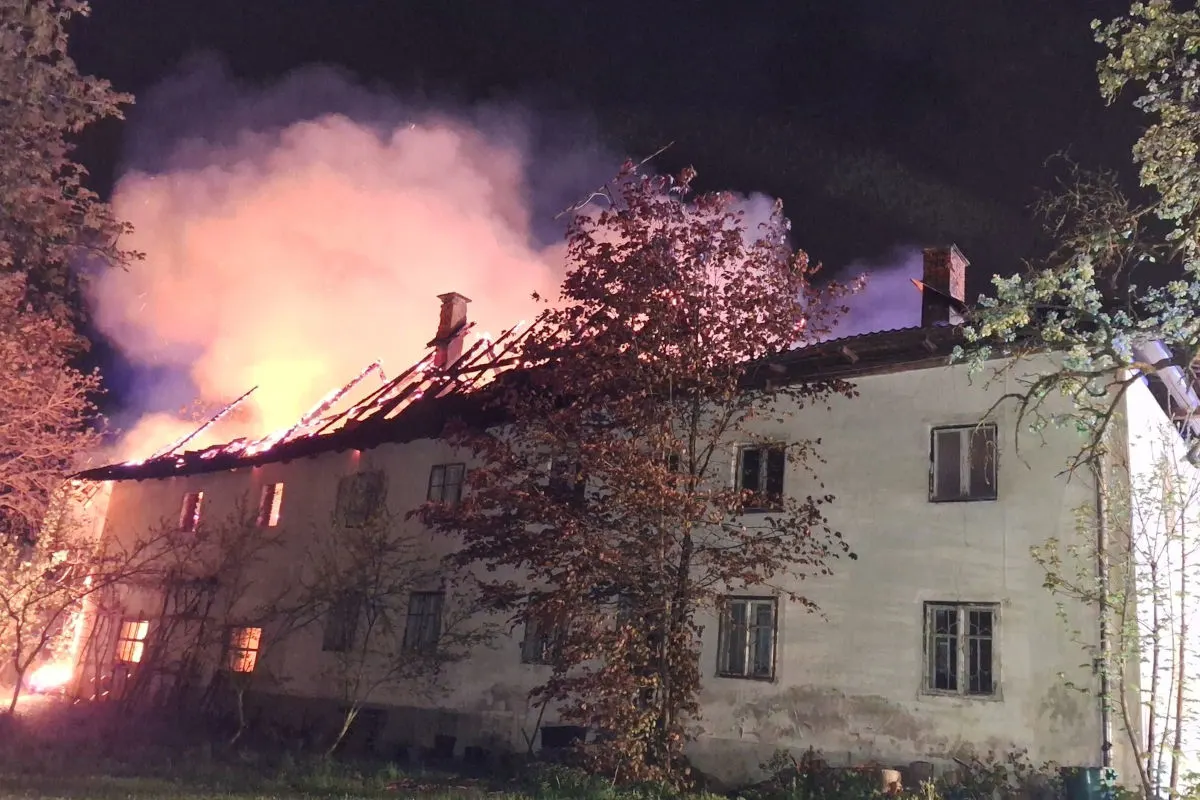 Ein großes, mehrstöckiges Gebäude steht nachts in Flammen. Das Dach ist größtenteils eingestürzt, und dichter Rauch steigt auf.