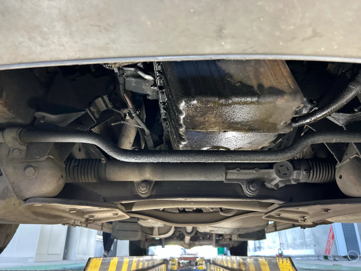 Die Unterseite eines Fahrzeugs zeigt deutliche Ölrückstände; das Fahrzeug befindet sich auf einer Hebebühne, um mögliche Schäden zu untersuchen.