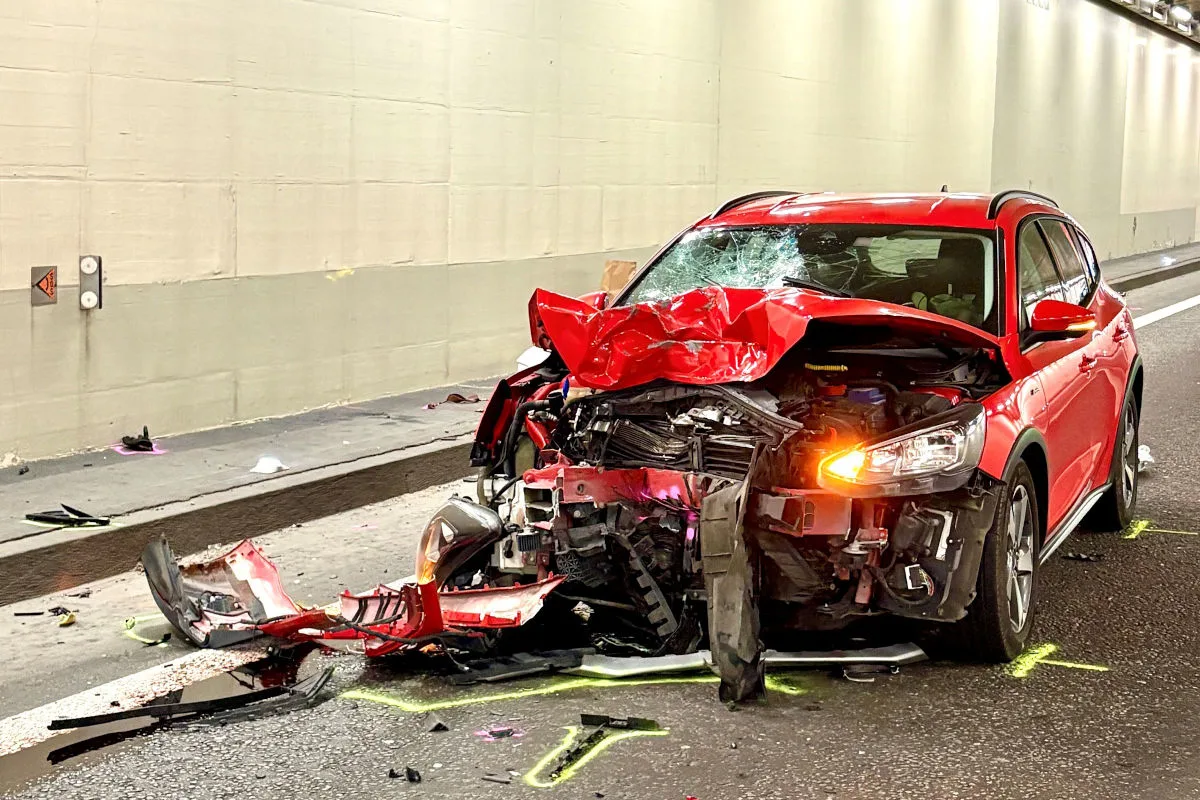 Das Bild zeigt ein rotes Auto mit erheblichen Frontschäden. Es steht still in einem Tunnel, umgeben von Trümmern.