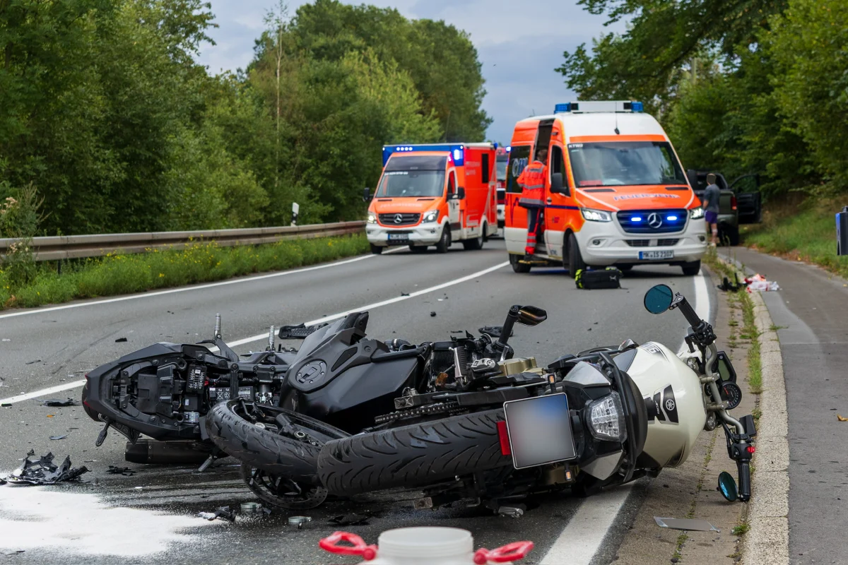 Zwei Motorräder liegen nach einem Unfall auf der Fahrbahn. Im Hintergrund sind zwei Rettungswagen zu sehen.