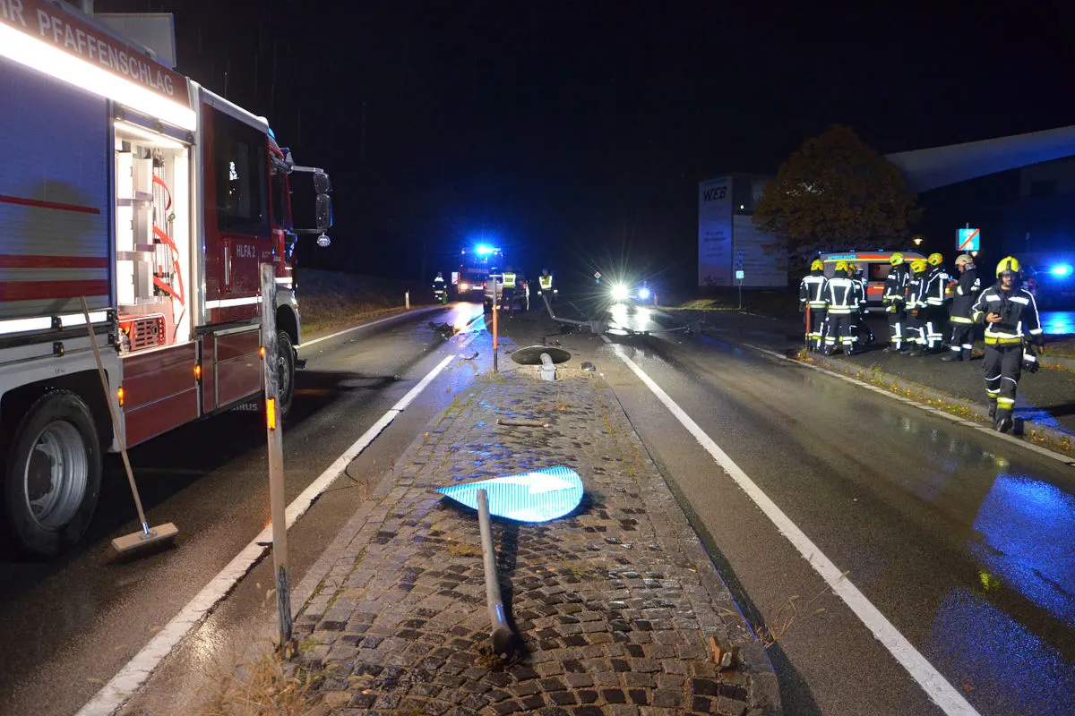 Ein Feuerwehrfahrzeug steht mit geöffnetem Equipment auf einer nächtlichen Landstraße, während Einsatzkräfte vor Ort sind und ein umgekipptes Verkehrsschild sichtbar ist.