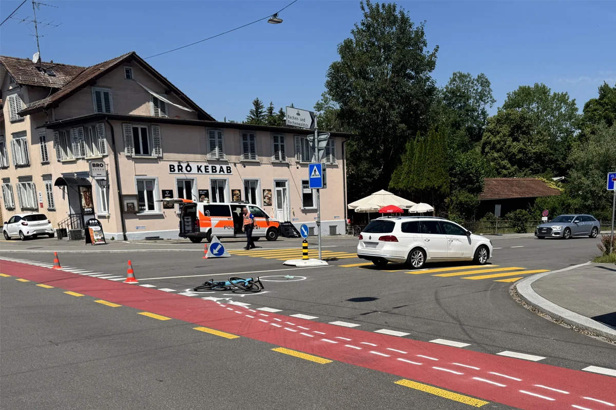 An einer Kreuzung liegt ein umgestürztes Fahrrad auf der Straße. Ein Polizeifahrzeug ist am Straßenrand geparkt, während ein Beamter die Umgebung sichert.