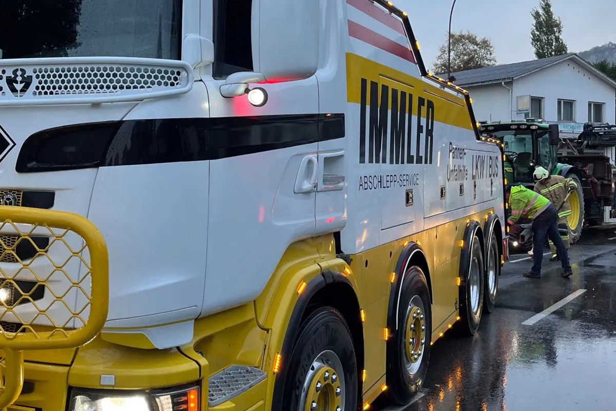 Ein großes Abschleppfahrzeug mit der Aufschrift 'IMMLER Abschlepp-Service' steht bei einem Einsatz. Zwei Personen arbeiten daran, ein weiteres Fahrzeug abzuschleppen.