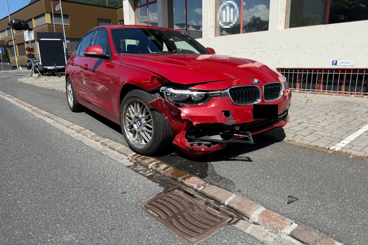 Ein roter BMW steht mit heftigen Frontschäden am Straßenrand. Die rechte Frontpartie des Fahrzeugs ist stark eingedellt.
