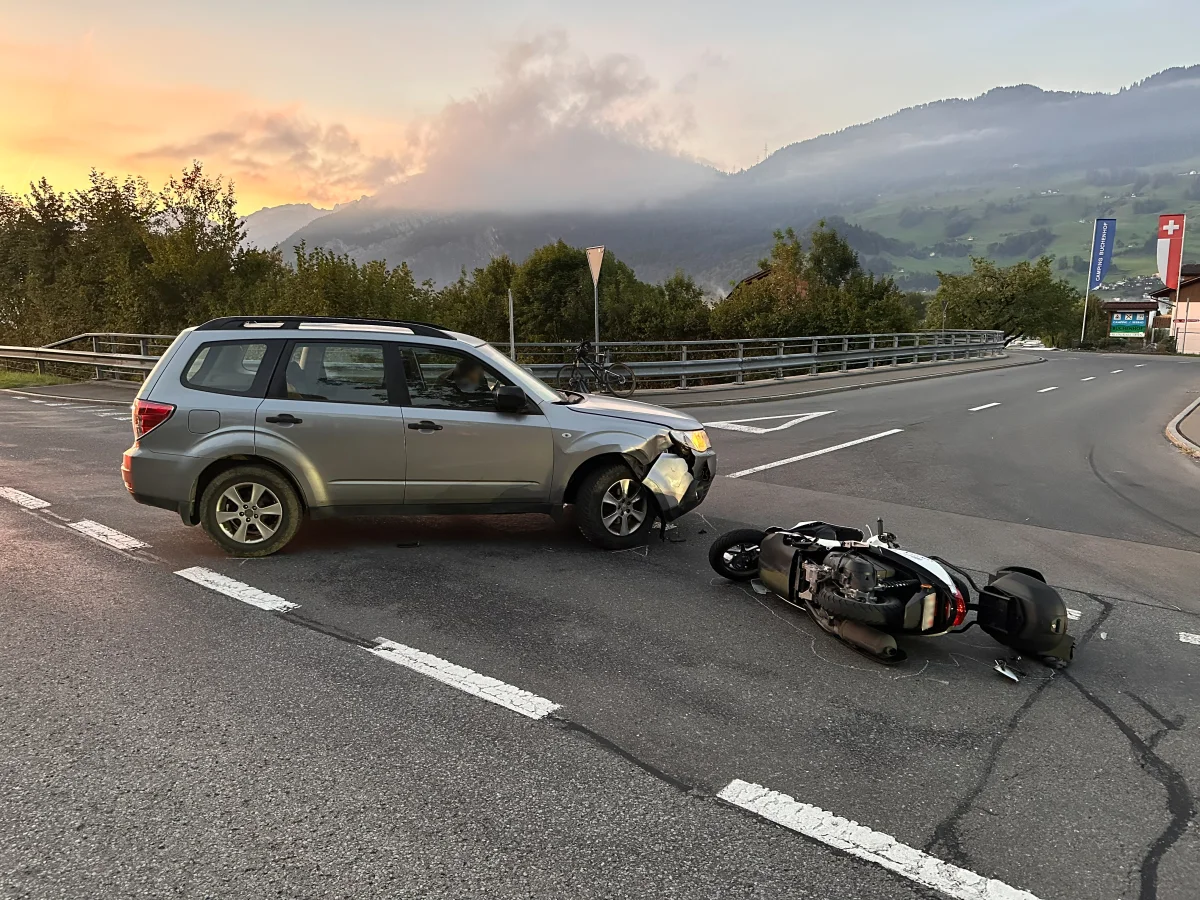 Ein silberner SUV zeigt erhebliche Frontschäden, während ein Motorrad umgestürzt auf der Straße liegt. Im Hintergrund ist eine hügelige Landschaft bei Sonnenuntergang zu sehen.