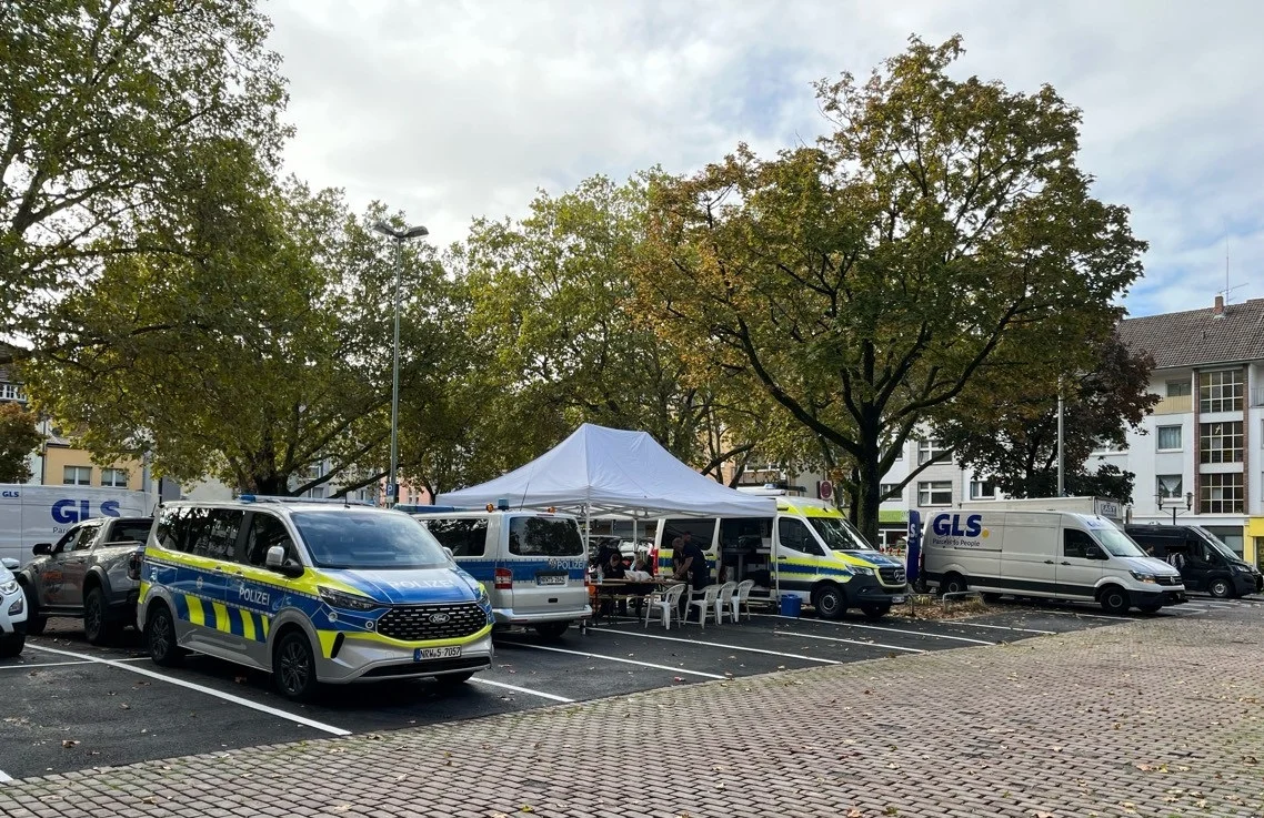 Mehrere Polizeifahrzeuge stehen auf einem Parkplatz neben einem mobilen Zelt. Der Himmel ist bewölkt und einige Bäume sind zu sehen.