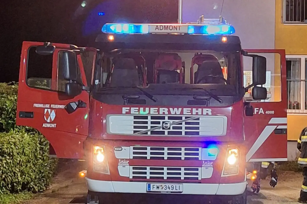 Ein rotes Feuerwehrfahrzeug der Freiwilligen Feuerwehr Admont steht mit eingeschaltetem Blaulicht vor einem Gebäude in der Nacht. Die Türen des Fahrzeugs sind geöffnet.