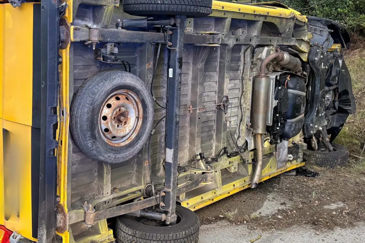 Ein gelber Transporter liegt seitlich an einem Straßenrand. Der Unterboden ist gut sichtbar, das Fahrzeug scheint beschädigt zu sein.