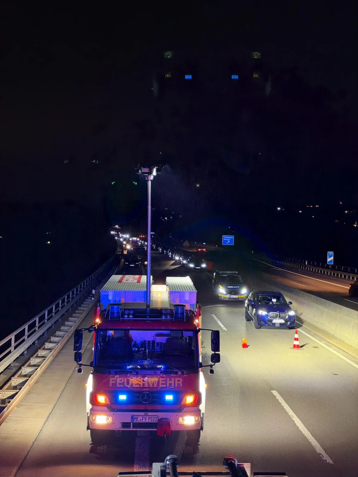 Ein Feuerwehrfahrzeug steht mit eingeschaltetem Licht auf einer nächtlichen Autobahn. Andere Fahrzeuge sind ebenfalls sichtbar.