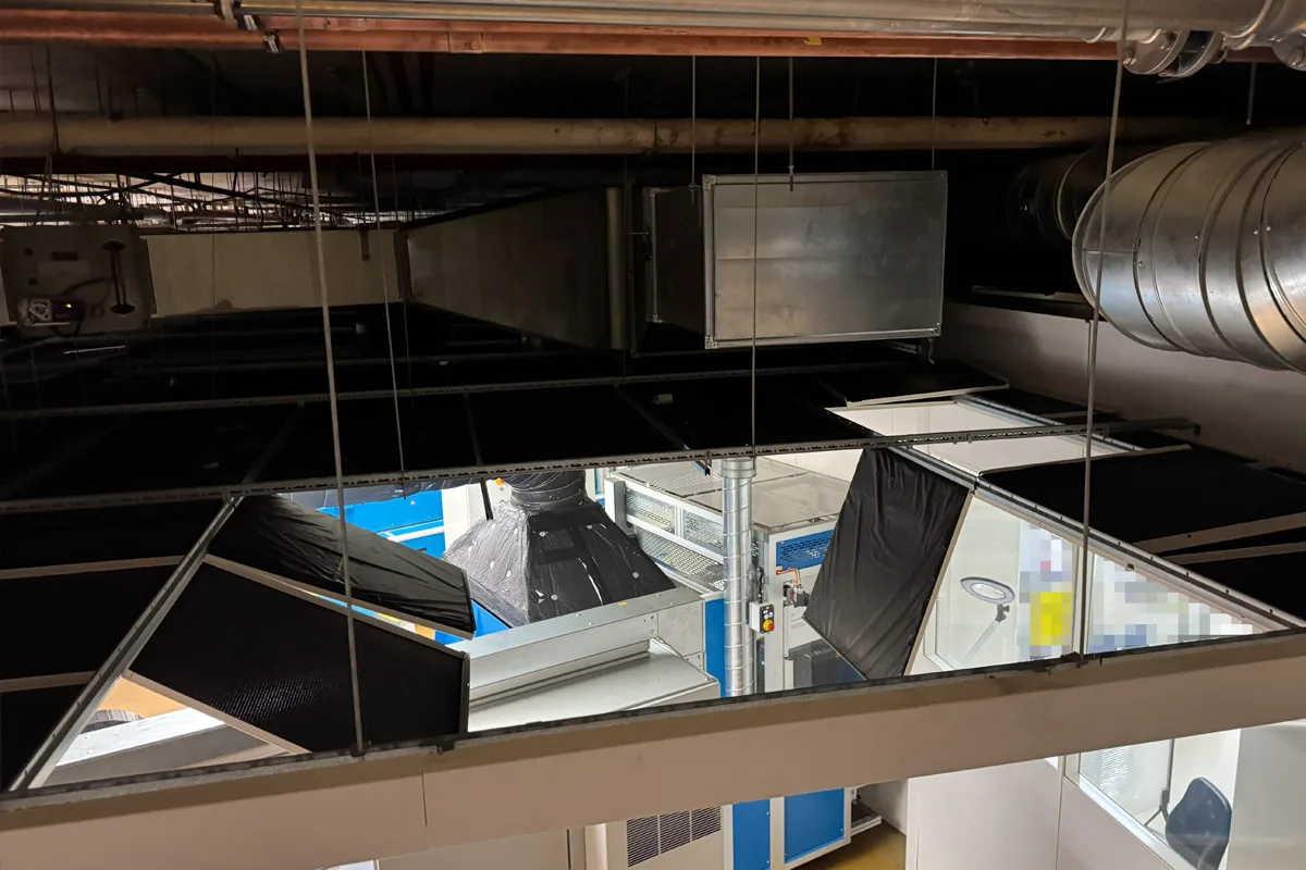 Eine Deckenverkleidung in einer Industrieanlage ist eingestürzt, wodurch Kabel und Lüftungssysteme sichtbar werden.