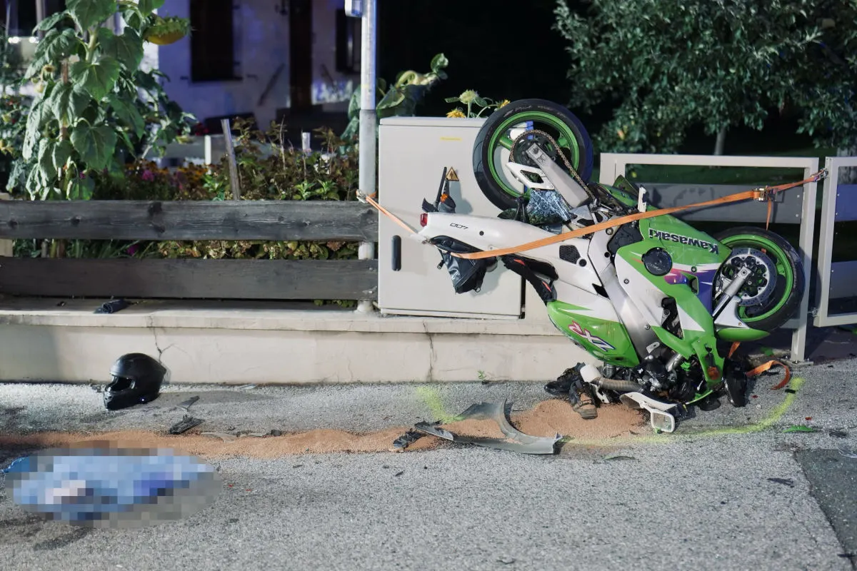 Ein grünes Motorrad liegt umgestürzt auf einem Gehweg neben einer Straße, umgeben von Trümmern und einem Motorradhelm.