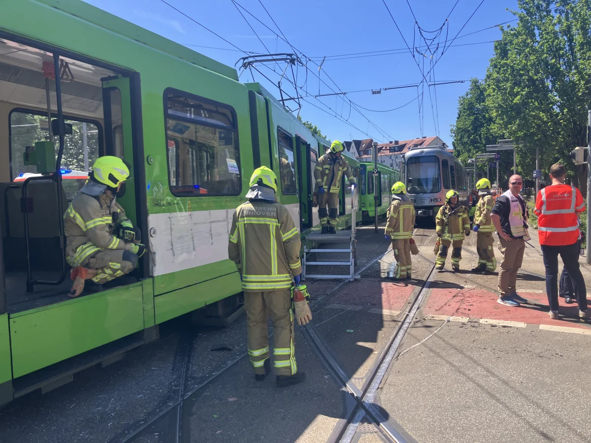 Mehrere Feuerwehrleute in Schutzkleidung stehen neben einer grünen Straßenbahn und überprüfen die Situation.