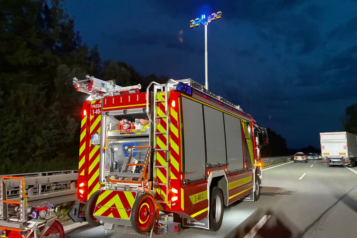 Ein rotes Feuerwehrfahrzeug steht auf einer beleuchteten Autobahn bei Nacht, mit geöffneten Stauräumen auf der Rückseite.