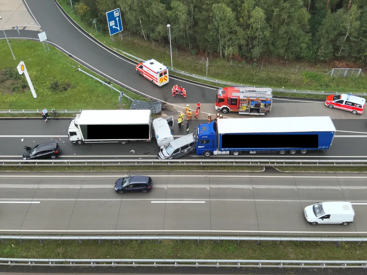 Ein Kleintransporter ist zwischen zwei Lastwagen auf einer Autobahn eingeklemmt. Rettungsfahrzeuge und Einsatzkräfte sind vor Ort.