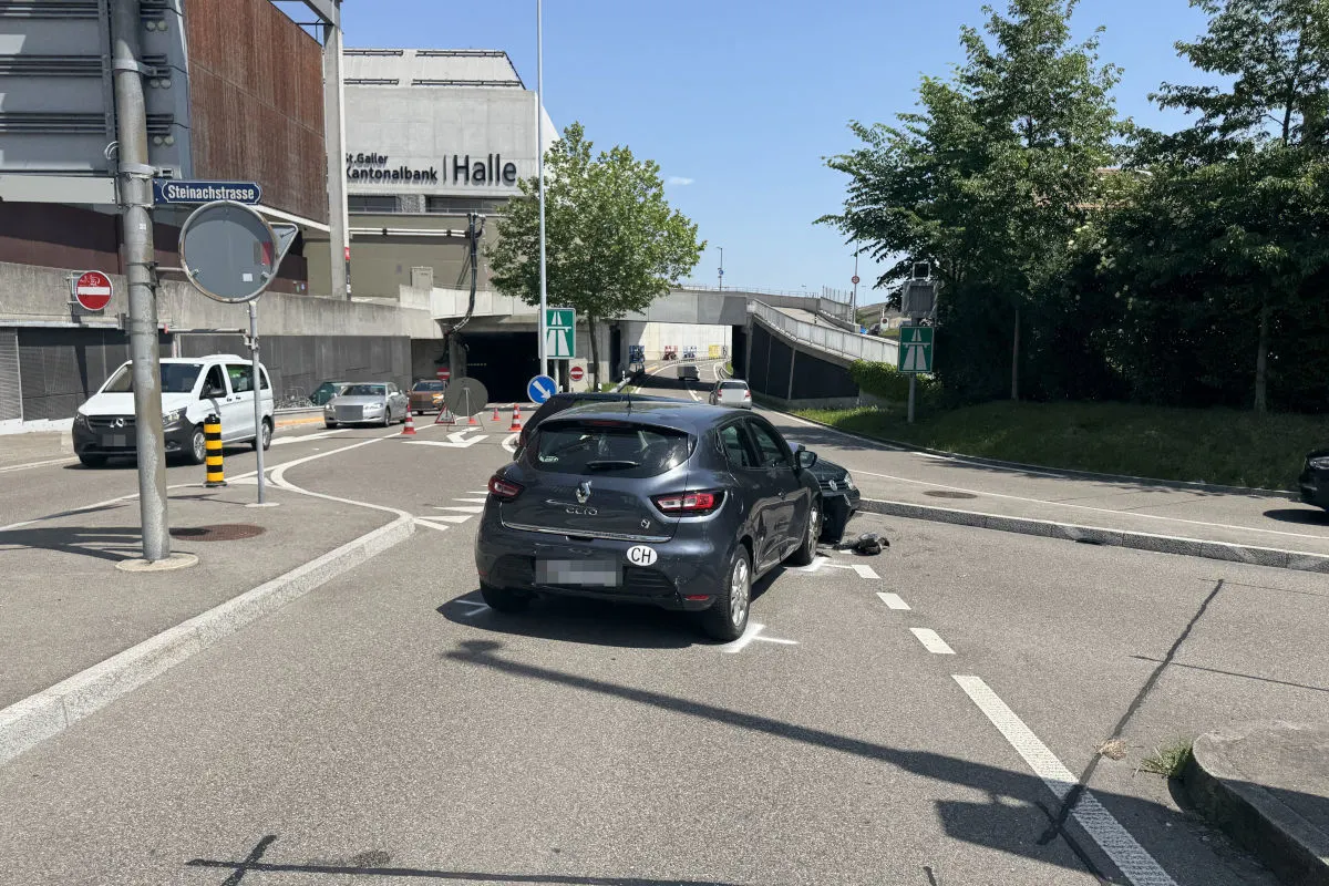 Ein schwarzer Renault Clio steht mitten auf einer Straße in der Nähe einer Kollision mit einem Motorrad. Im Hintergrund sind andere Fahrzeuge und ein Gebäude sichtbar.