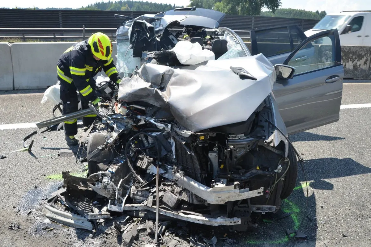 Ein Feuerwehrmann bearbeitet die Spitze eines massiven Autowracks auf der Autobahn. Das Auto ist stark deformiert und zerstört.