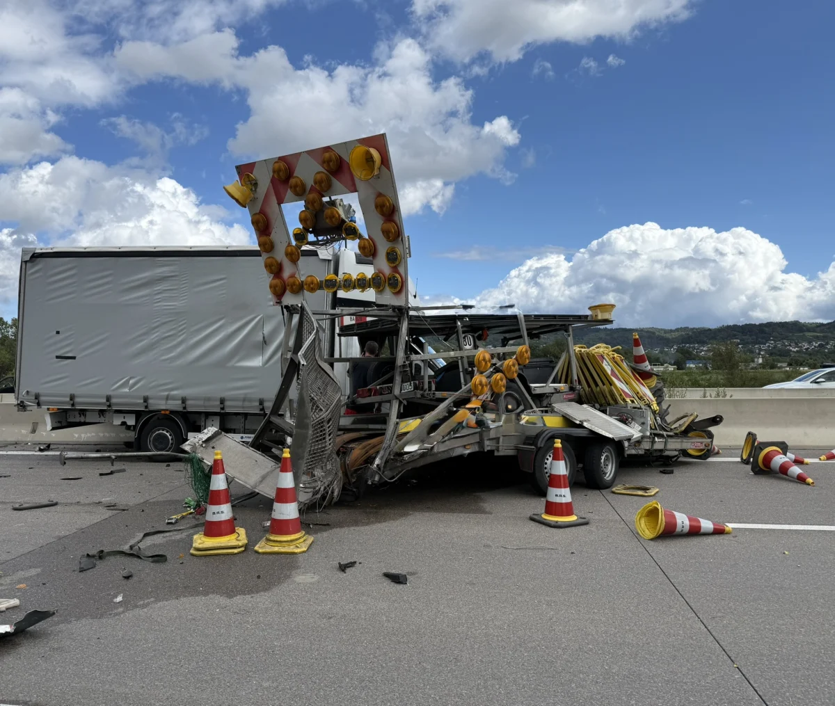Auf einer Autobahn steht ein schwer beschädigtes Absicherungsfahrzeug, das vor einen Lkw geprallt ist. Trümmer und Verkehrshütchen liegen verstreut auf der Fahrbahn.