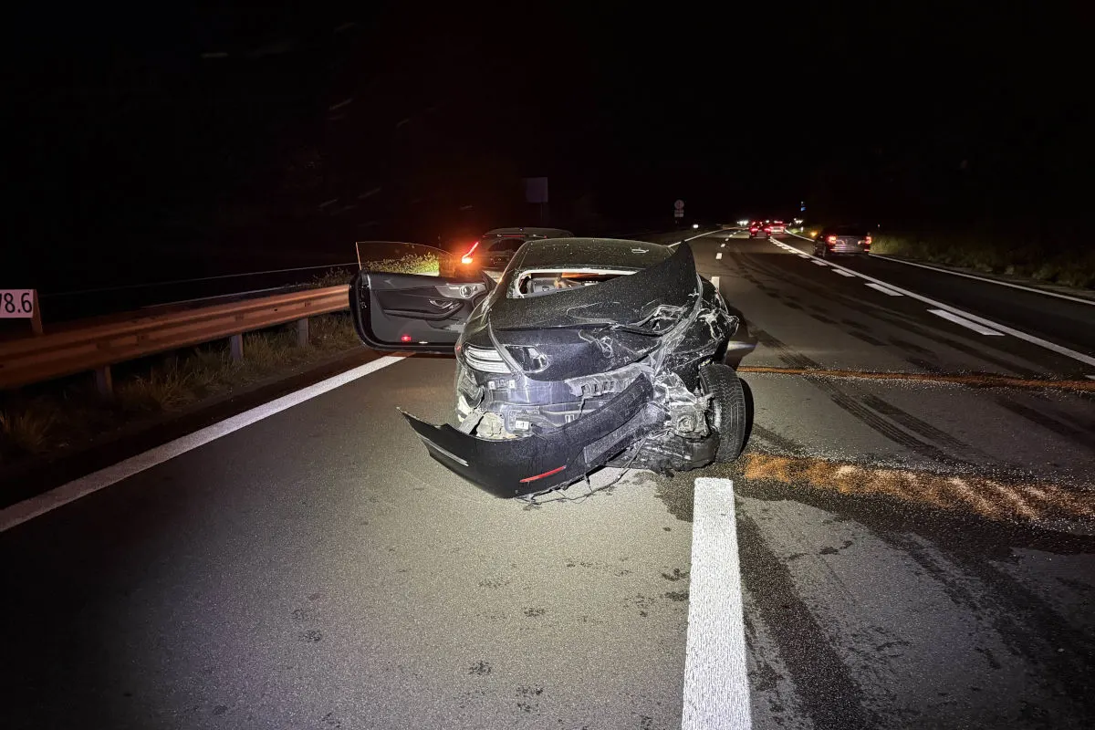 Ein stark beschädigtes Auto steht auf einer Autobahn. Die Front ist stark eingedrückt, und die Szene ist bei Nacht aufgenommen.
