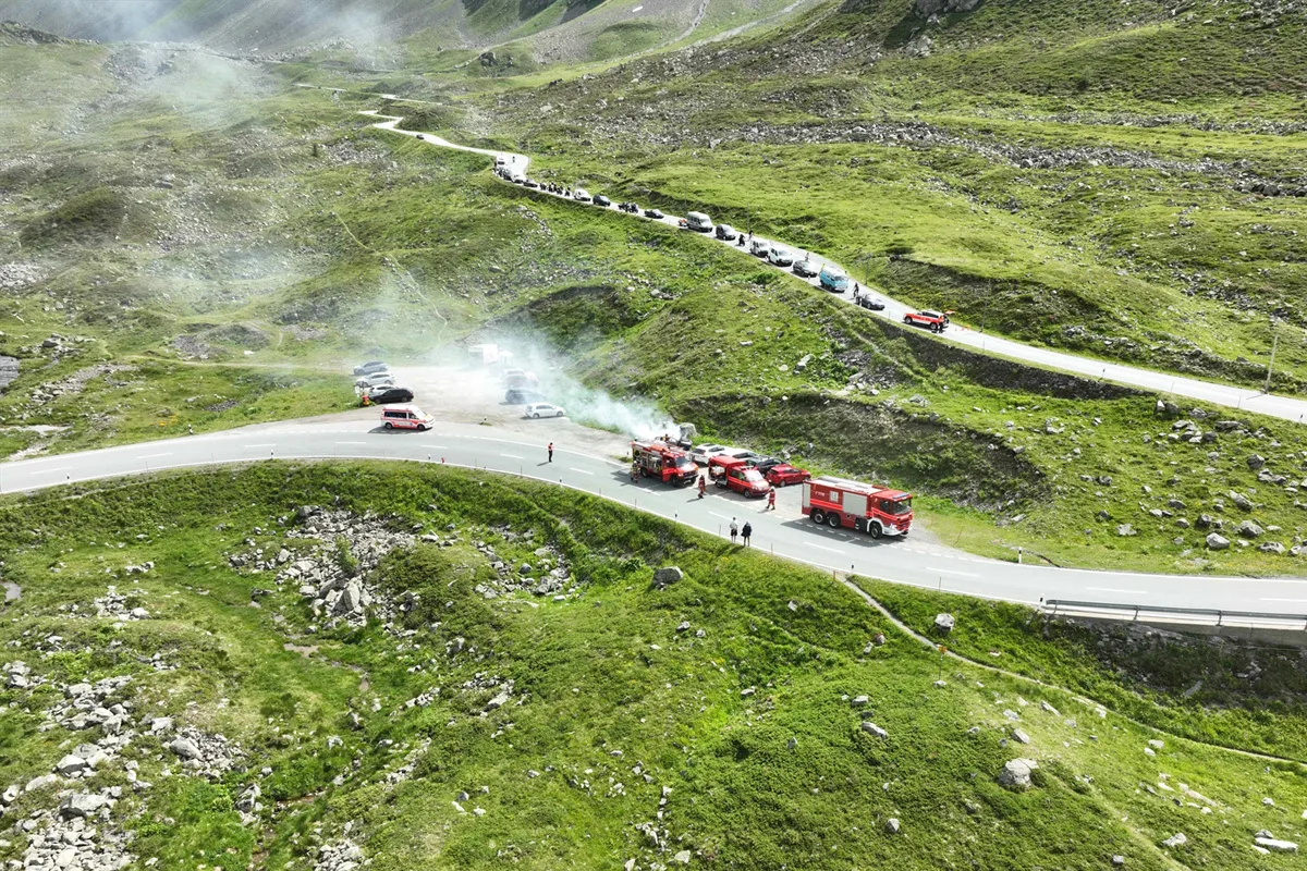 Eine Bergstraße mit mehreren Feuerwehrfahrzeugen, die einen Einsatz durchführen. In der Nähe ist Rauch sichtbar, was auf einen Brand hindeutet.