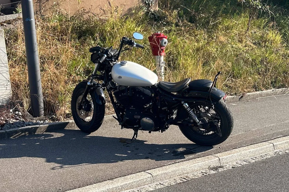 Ein schwarzes Motorrad mit weißem Tank steht geparkt am Straßenrand. Im Hintergrund ist ein roter Hydrant sichtbar.