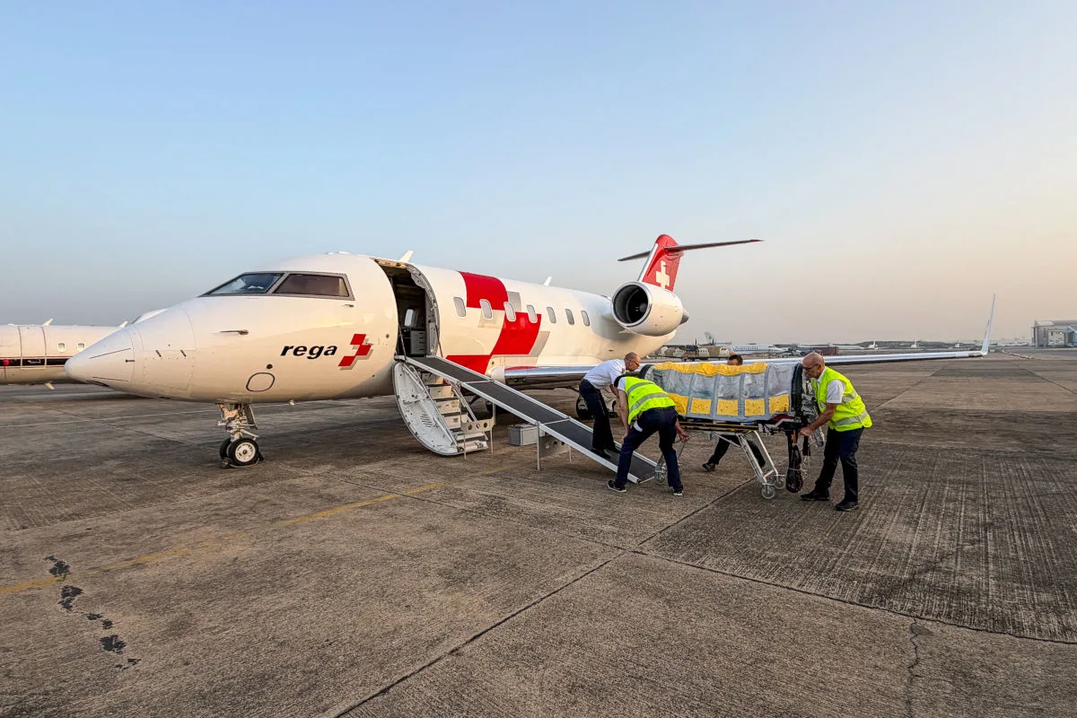 Ein Ambulanzjet der Rega steht auf einem Flugfeld. Drei Personen in Warnwesten positionieren eine Trage über eine Rampe in das Flugzeug.