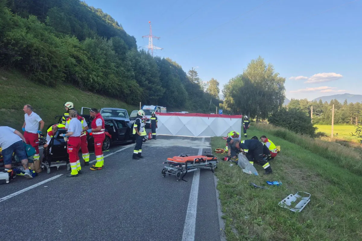 Rettungskräfte und mehrere Personen sind an einer Unfallstelle auf einer Landstraße beschäftigt. Ein Rettungswagen und Geräte sind sichtbar.