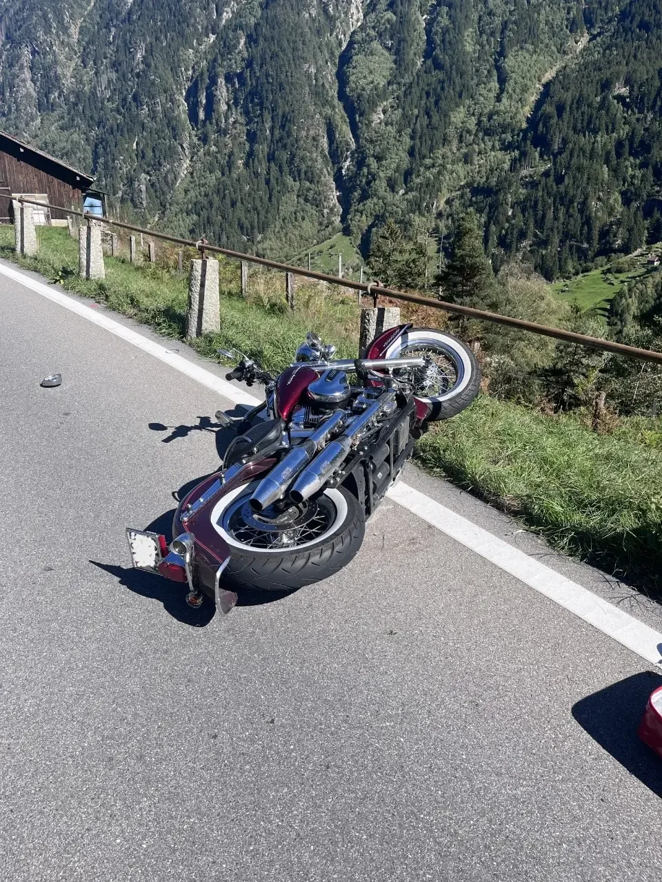 Ein Motorrad liegt auf einer kurvenreichen Bergstraße in den Bergen. Die Szene zeigt eine Berglandschaft mit grünen Hängen und einem sonnigen Himmel.