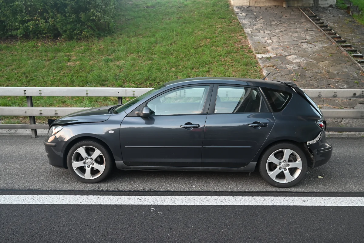 Ein schwarzer Pkw steht am Seitenstreifen der Autobahn mit sichtbarem Heckschaden in ländlicher Umgebung.