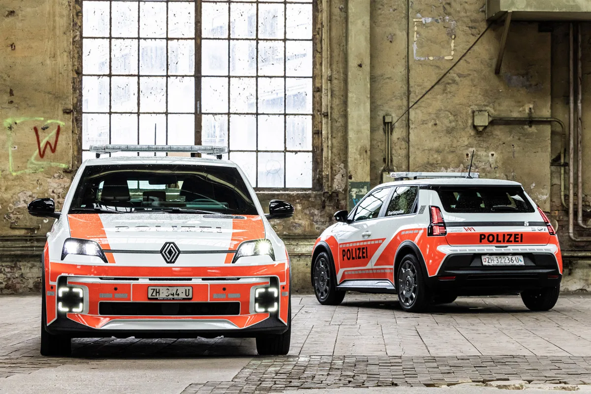 In einer alten Industriehalle stehen zwei orange-weiße Polizeiautos. Eines zeigt die Front, das andere die Rückseite.